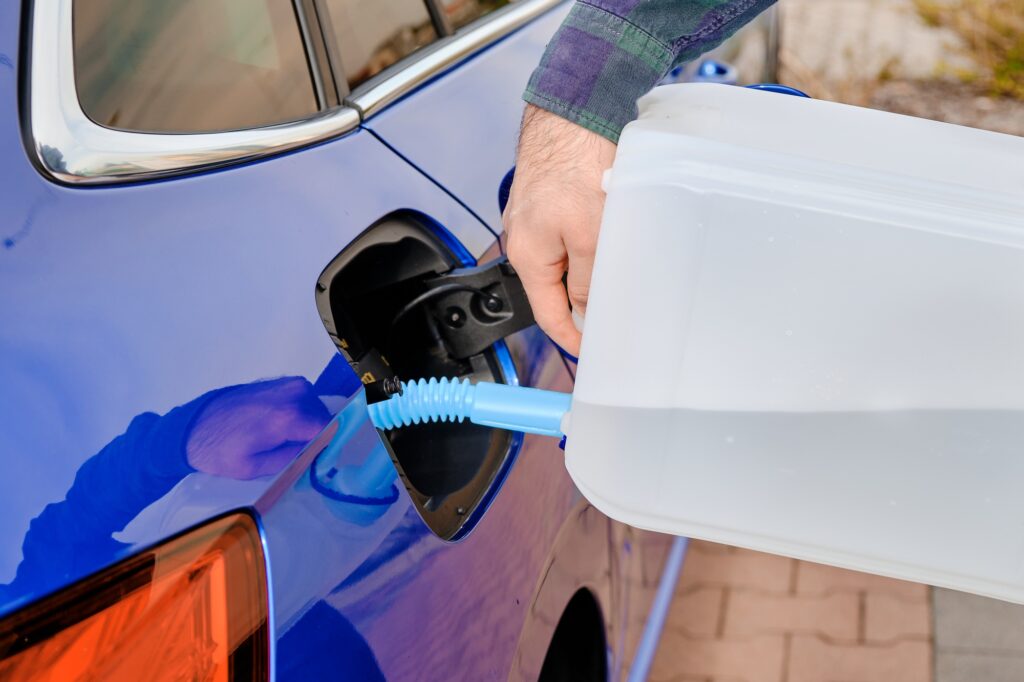 Close up man filling a diesel engine fluid from canister into the tank of blue car. Diesel exhaust