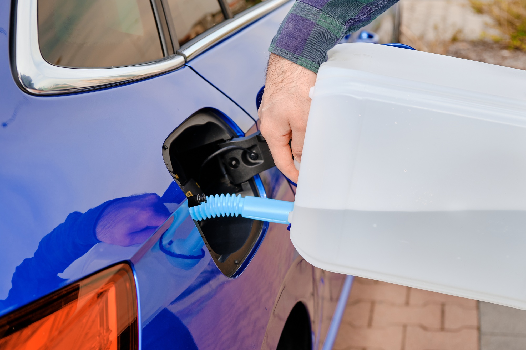 Close up man filling a diesel engine fluid from canister into the tank of blue car. Diesel exhaust